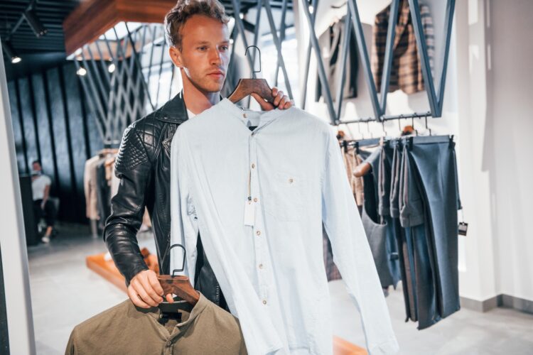 Big choice. Young guy in modern store with new clothes. Elegant expensive wear for men