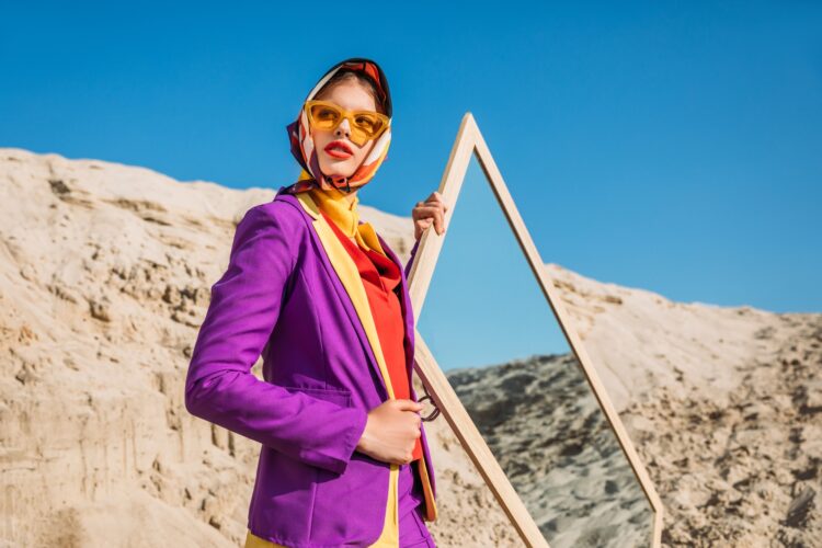 beautiful elegant model in fashionable clothes posing near mirror on sand dune