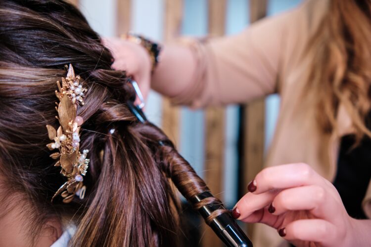 Hairstylist curling a client hair while doing her wedding hairstyle at the hairdressing salon.