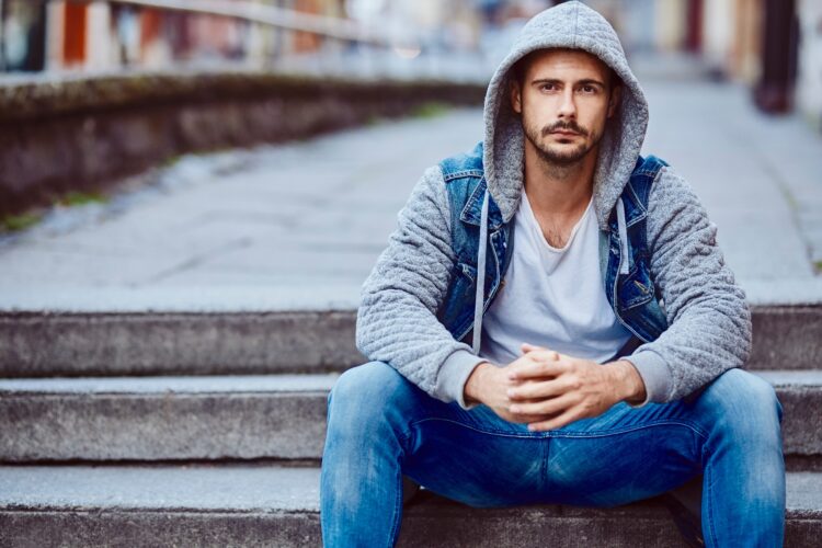 Serious man in hooded jacket sitting on stairs