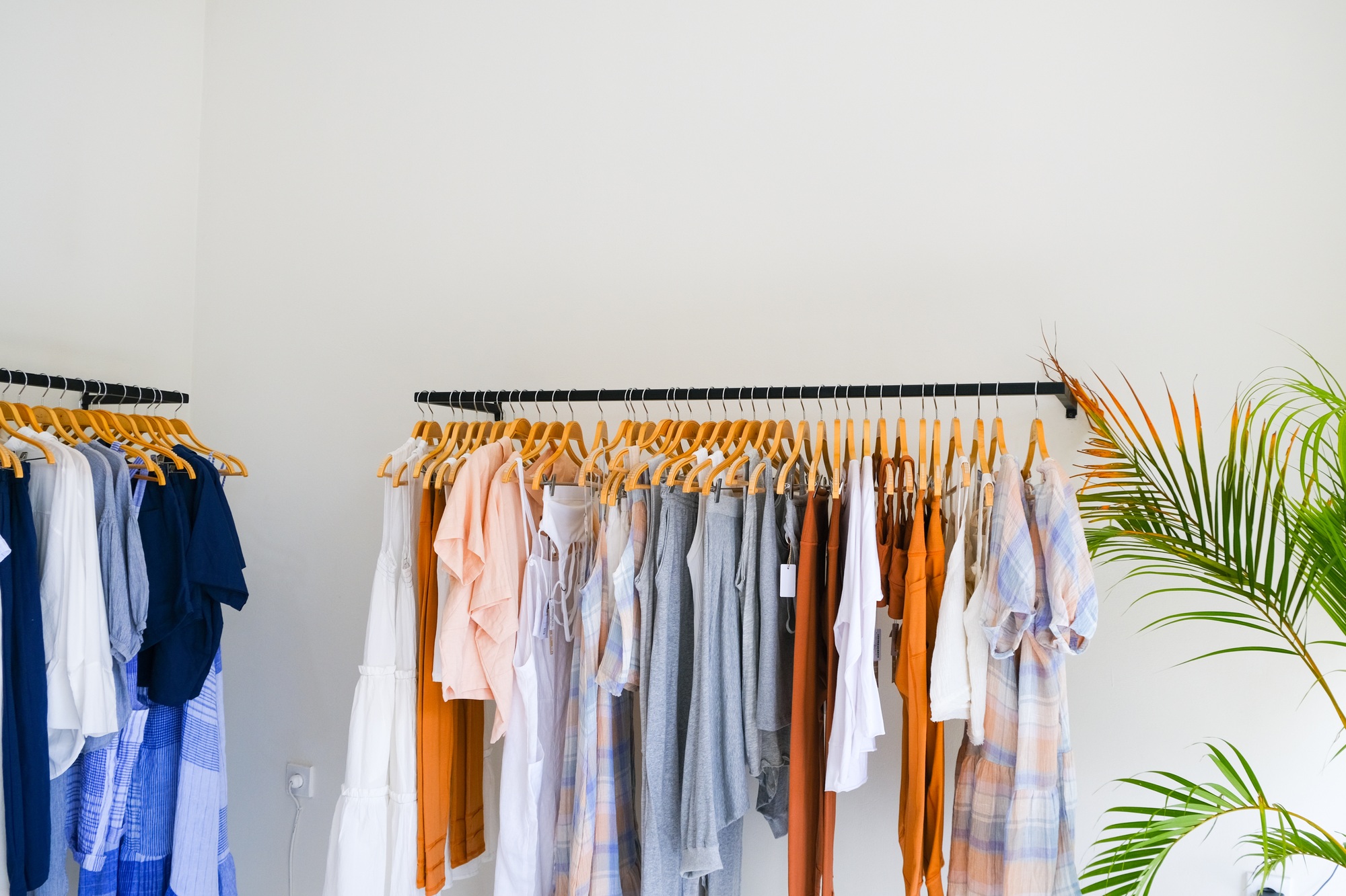 Two Racks of summer collection of natural clothes on hangers in retail fashion shop.