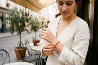 Femme portant un bracelet cordon tressé terracotta au poignet sur une robe lin crème dans un café parisien